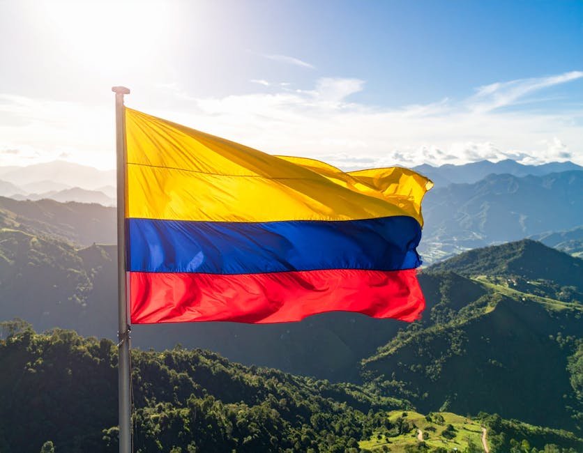 Vibrant Colombian flag waves against the backdrop of the Andes mountains under a bright sky.